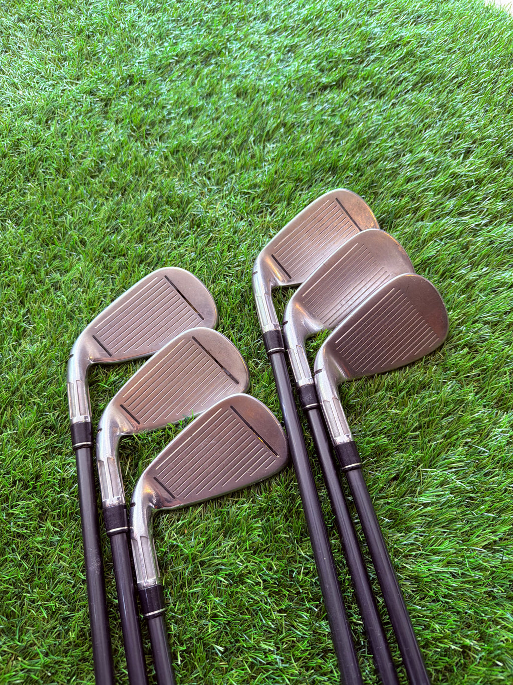 Rechtshandige TaylorMade M2 ijzers 5 tot PW met graphite shafts, golfclubs op een golfbaan met gras en clubs in de achtergrond