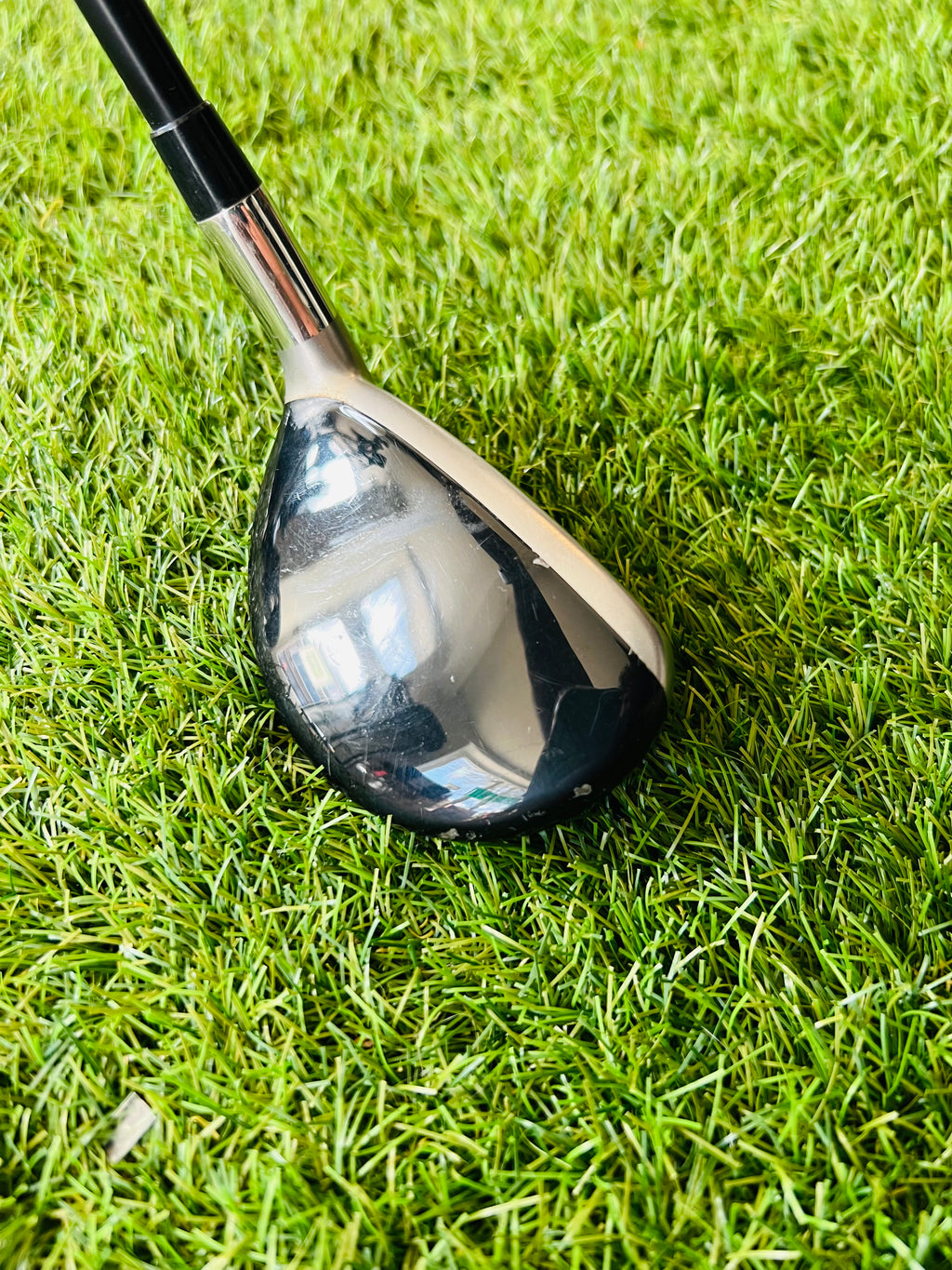 Rechtshandige Callaway RAZR X Tour hybride 2 met 18° loft, liggend op een golfbaan, met golfclubs en tee in beeld