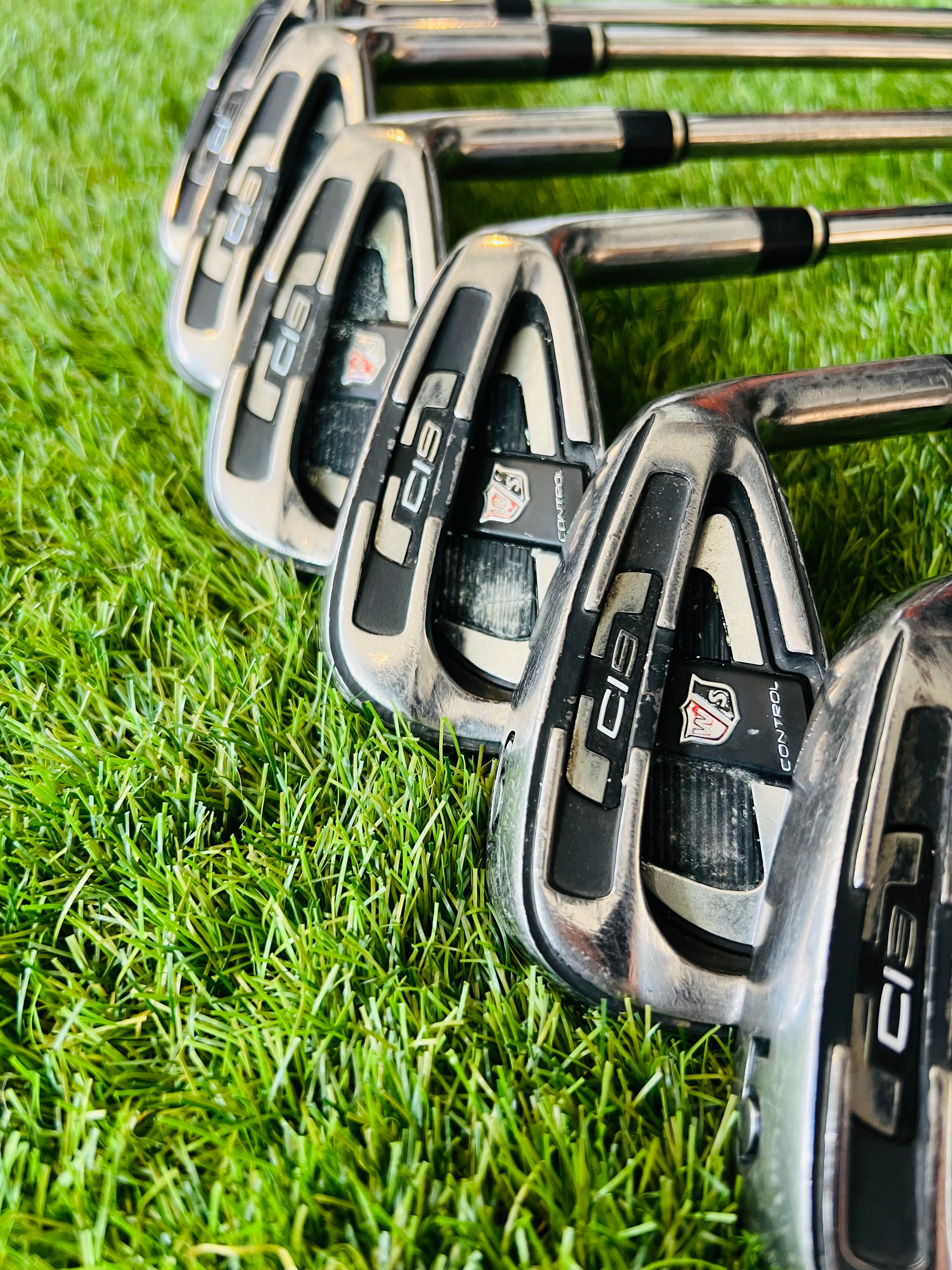 Rechtshandige Wilson Staff Ci9 golf ijzers 4 tot PW en GW op een golfclub met golfballen en tee op de achtergrond