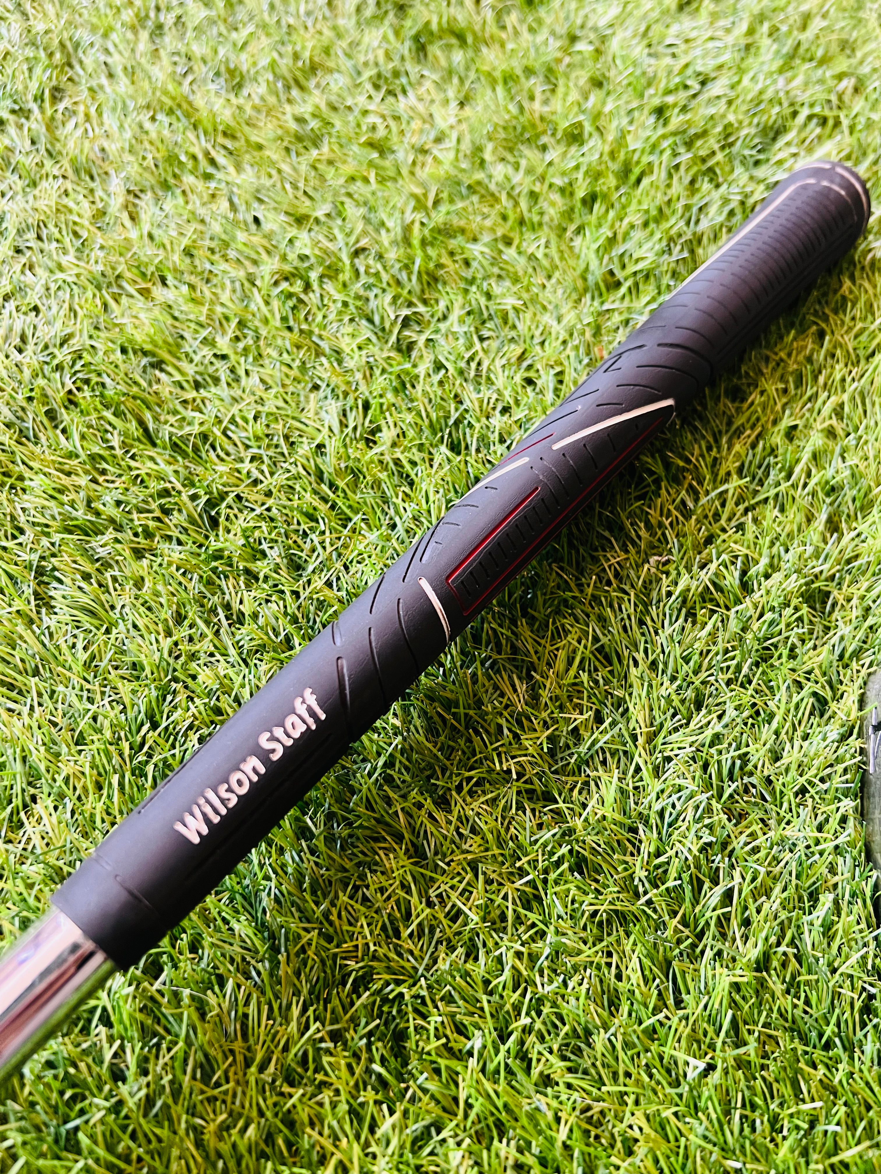 Rechtshandige Wilson Staff Ci9 golfclubs met ijzers 4 t/m PW en gap wedge, liggend op een golfbaan met bal en clubhoes.