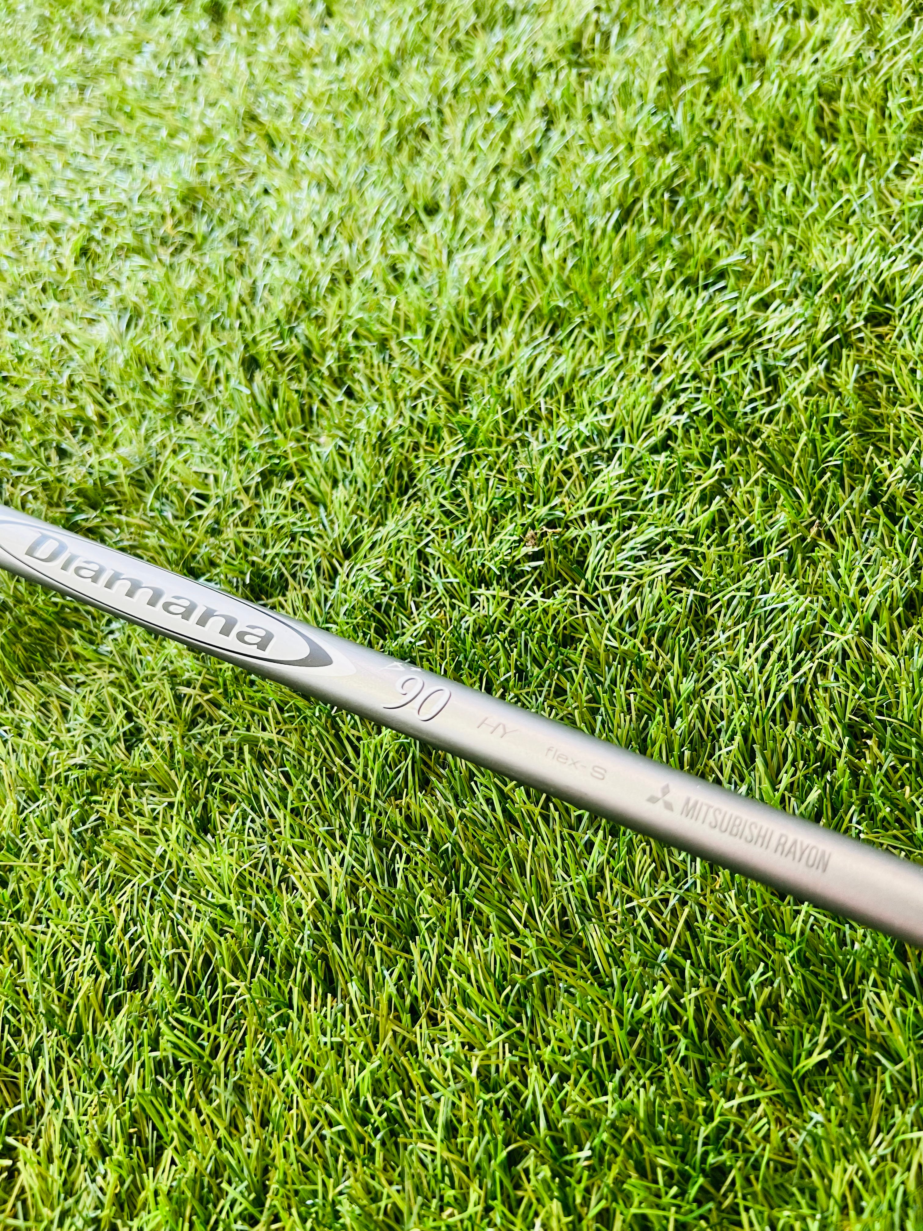 Titleist 915H hybride 2 met 17,5° loft, rechtshandig, gelegen op golfbaan met clubs en golfballen op de achtergrond