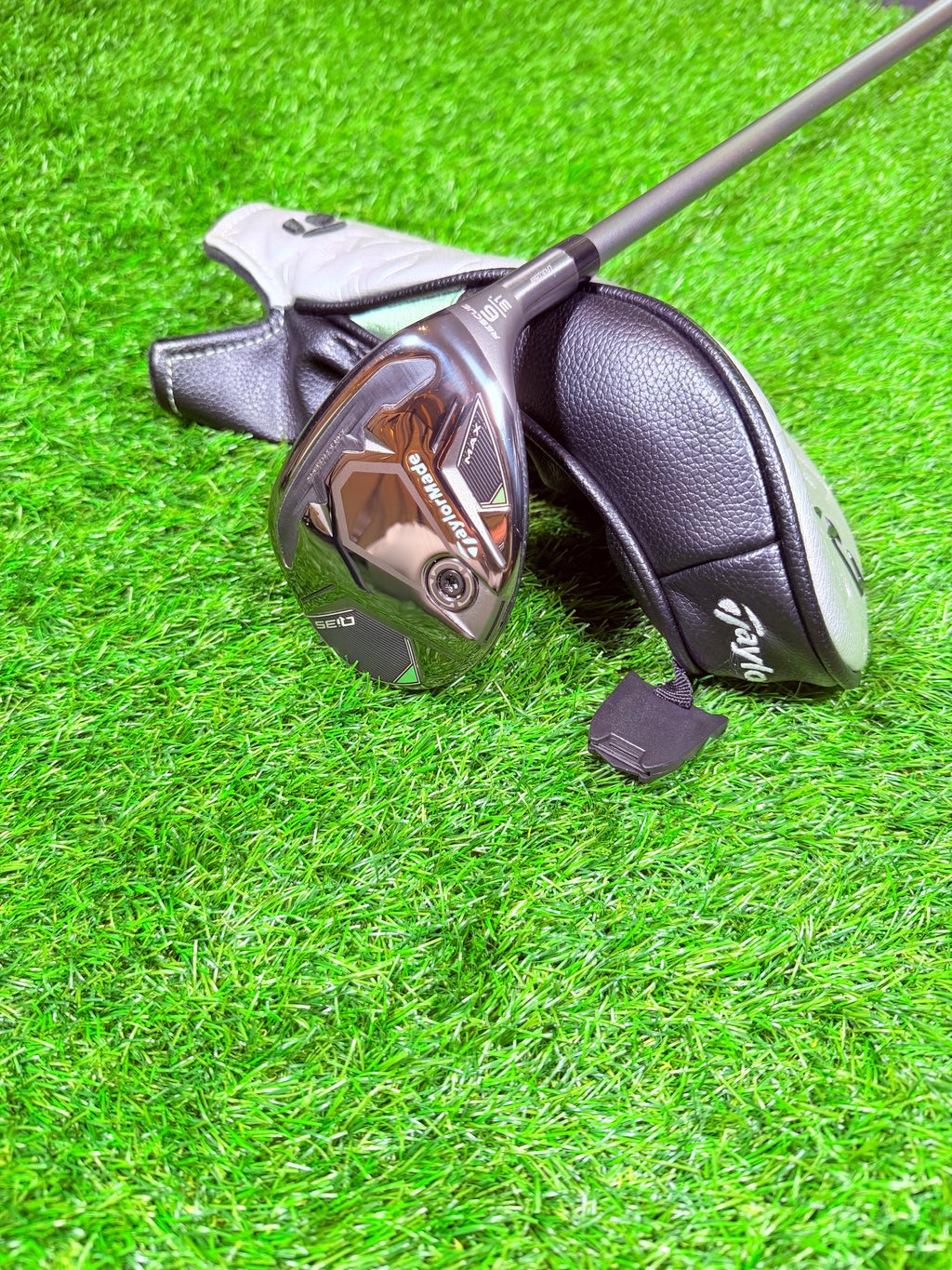 TaylorMade Qi35 Max hybride 6 (31°) voor rechtshandige golfers, liggend op een golfbaan met golfclubs op de achtergrond.