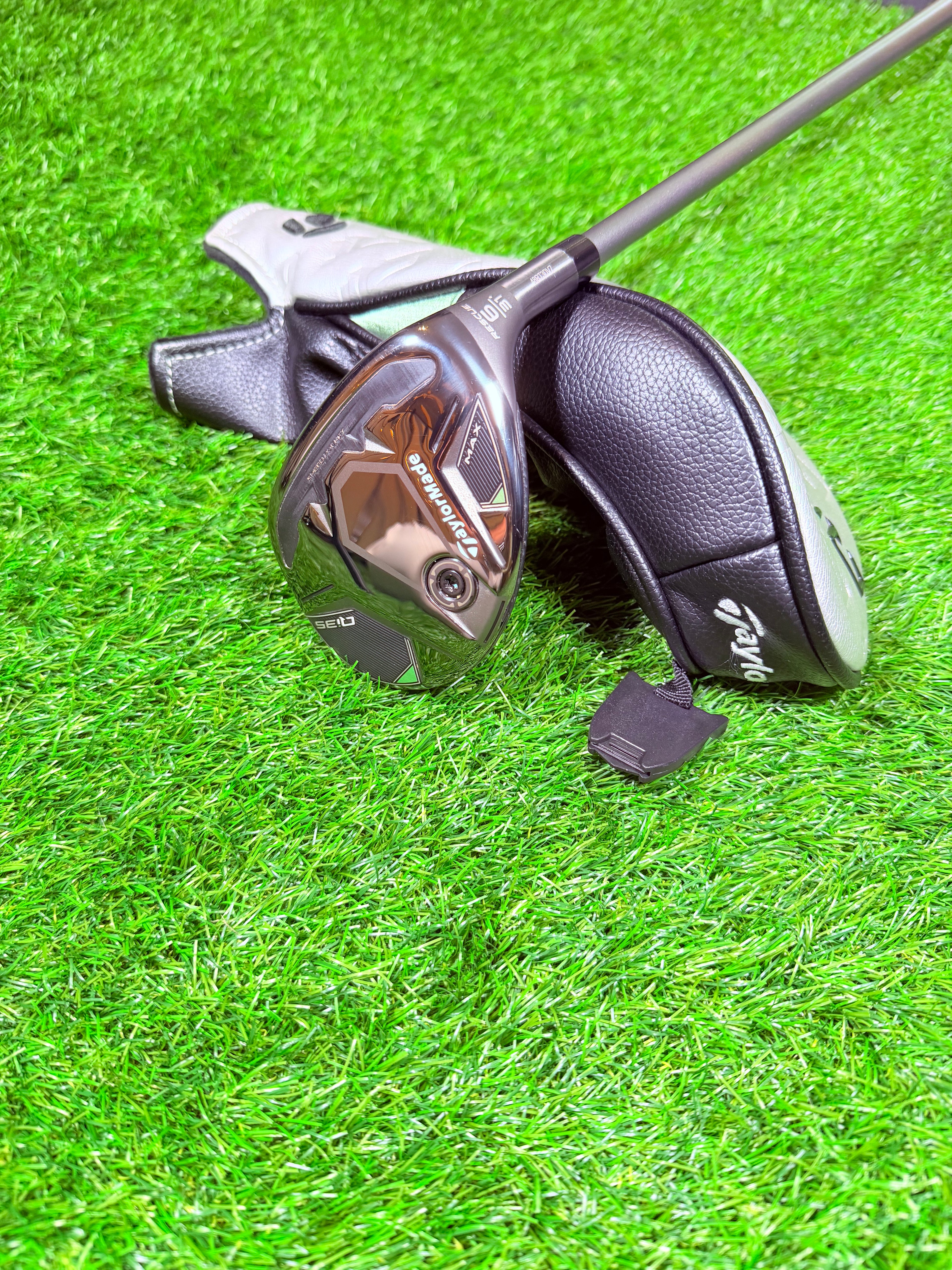 TaylorMade Qi35 Max hybride 6 (31°) voor rechtshandige golfers, liggend op een golfbaan met golfclubs op de achtergrond.