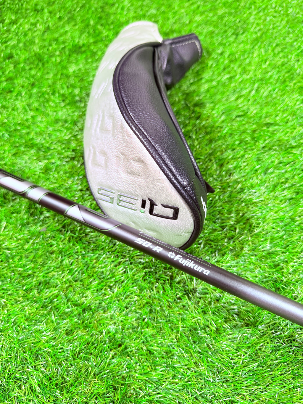 Rechtshandige TaylorMade Qi35 Max hybride 4 (23°) golfclub op een golfbaan, close-up van de clubhoofd en grip.