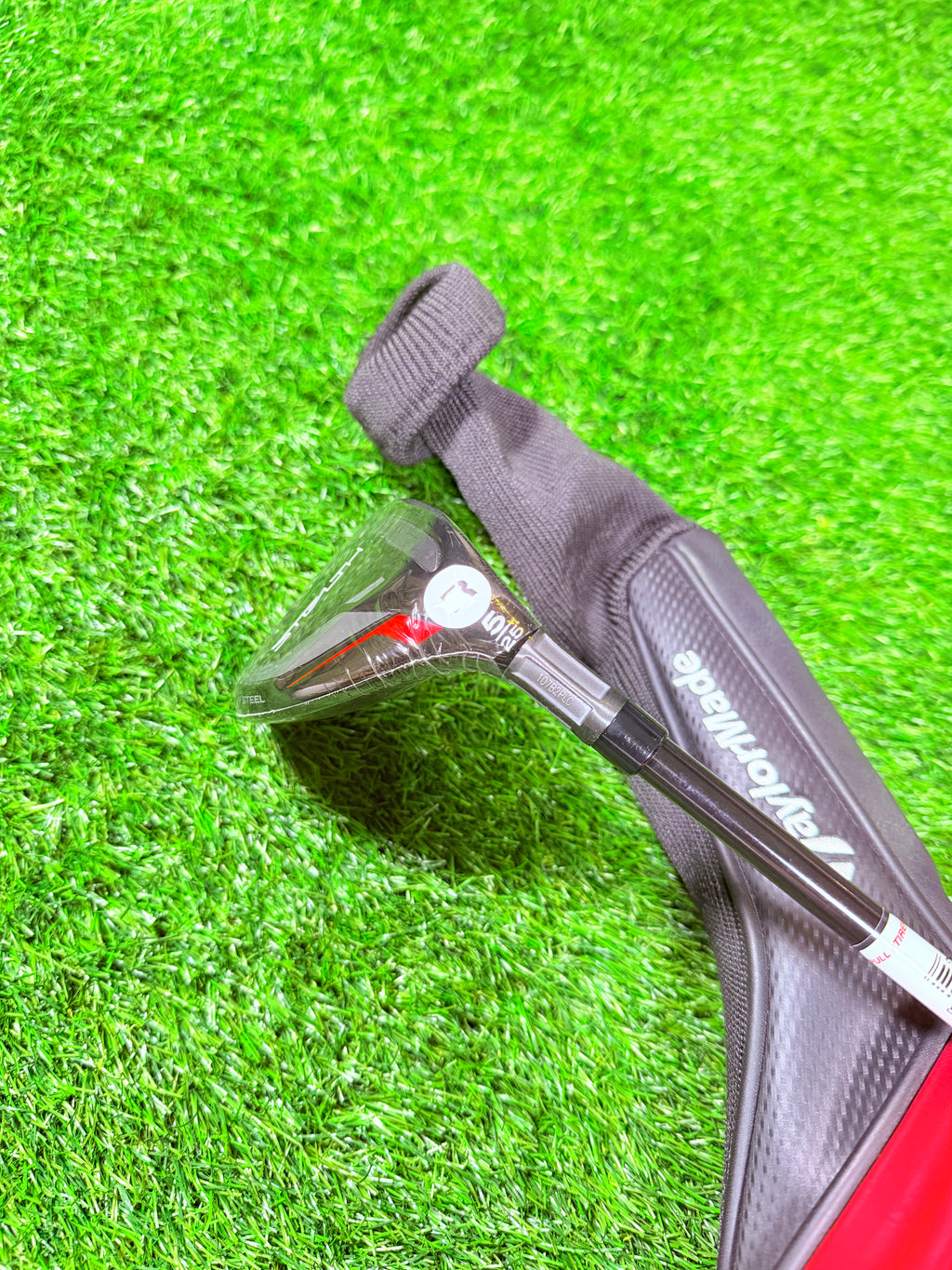 TaylorMade Stealth Hybride 5 (25°) golfclub, liggend op een groene fairway, zichtbaar met graphite shaft en zwarte clubkop.