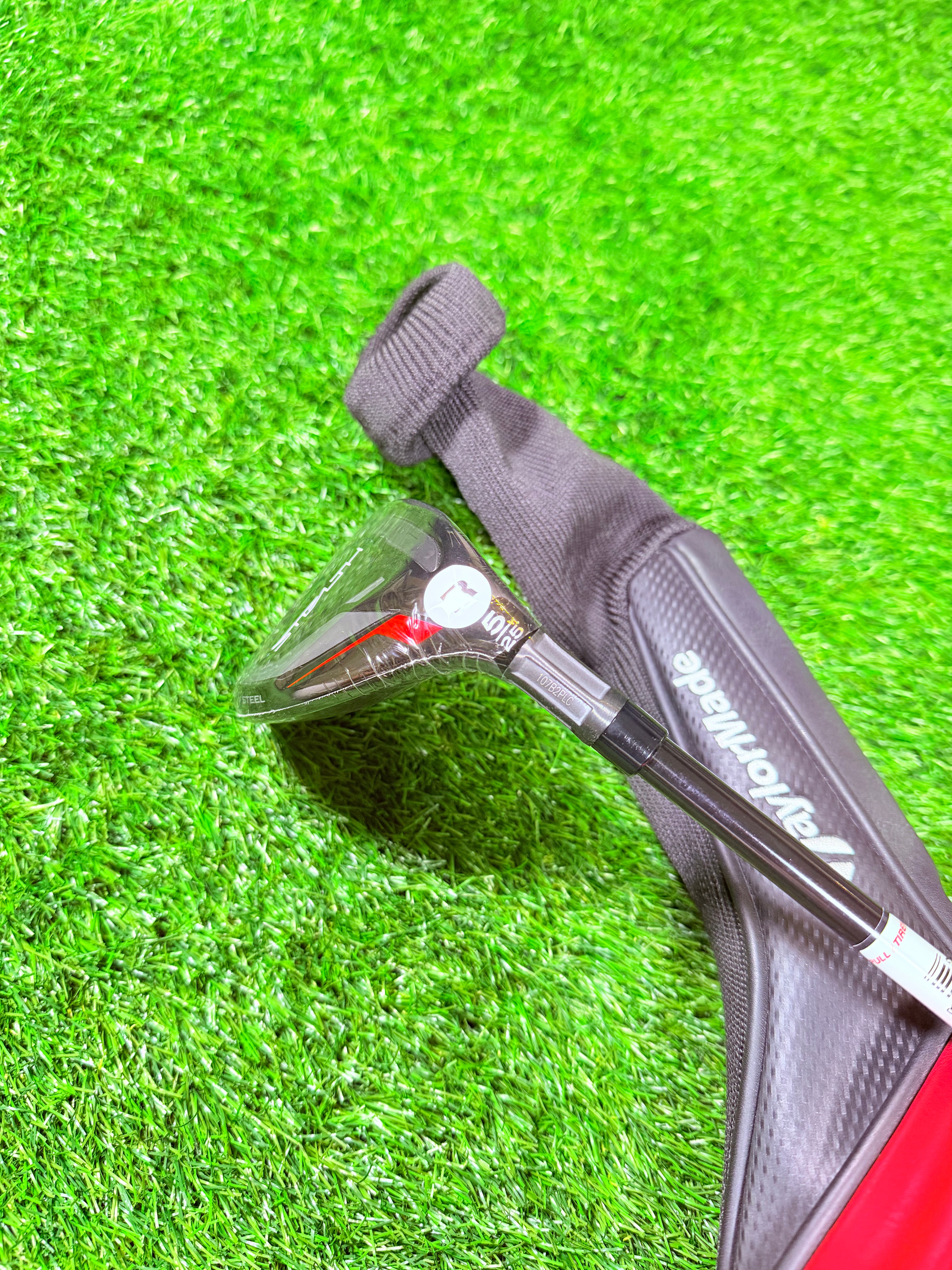 TaylorMade Stealth Hybride 5 (25°) golfclub, liggend op een groene fairway, zichtbaar met graphite shaft en zwarte clubkop.