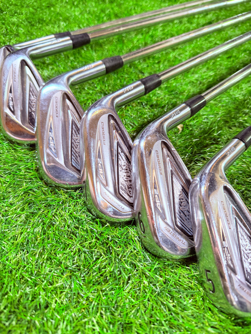 Titleist AP2 716 ijzerset 4 tot PW rechtshandig, close-up van de clubs met grip en clubkop op een golfbaan.