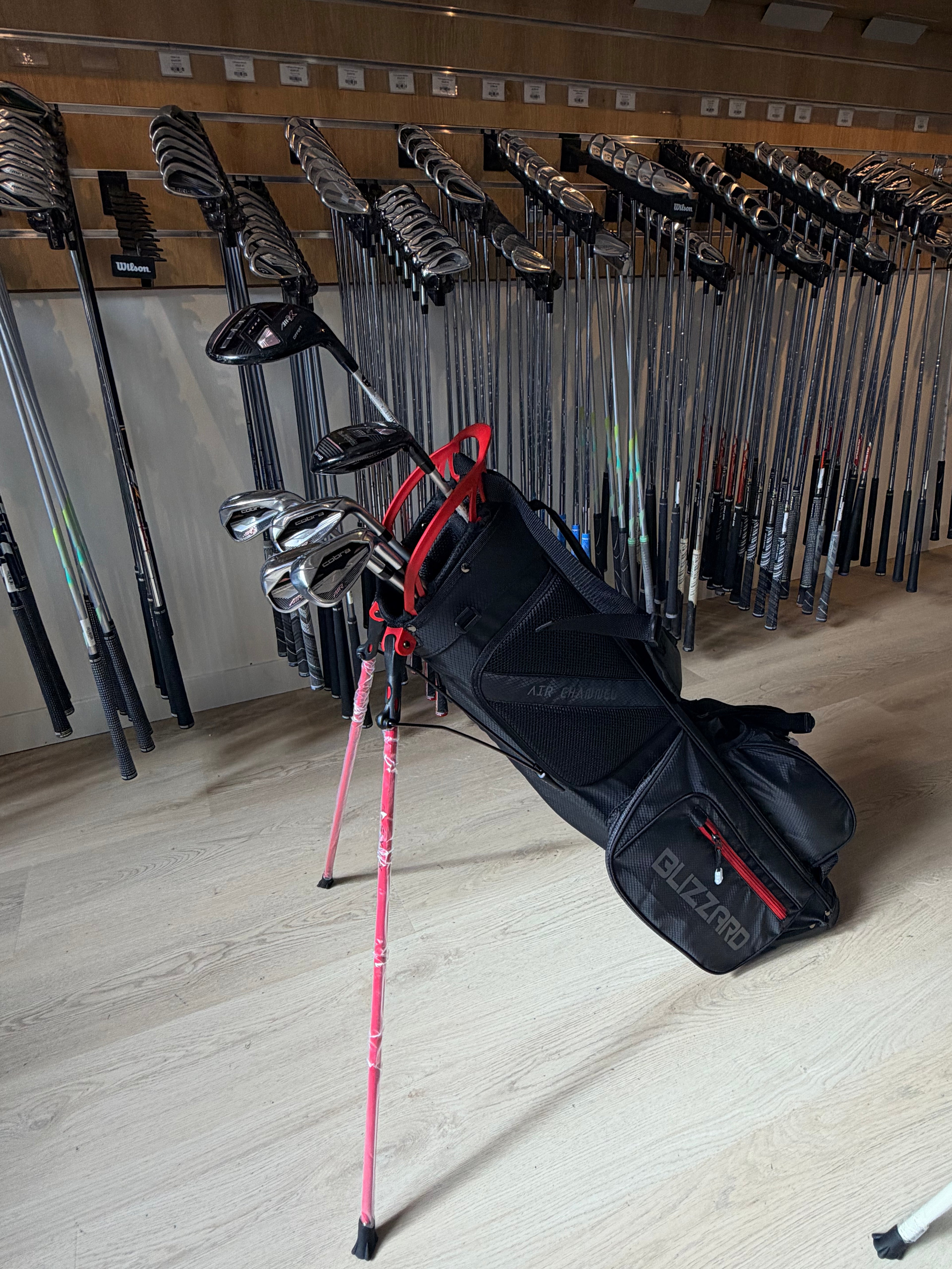 Cobra AIR-X dames golfset met 6 tot PW, hybride 5, 5-wood, putter en standbag, liggend op een golfbaan.